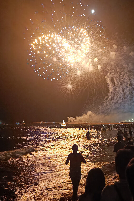 Fuengirola Virgen del Carmen festival in Los Boliches, fireworks on pier and people in the water and running from the beach into the water, the Virgin float in the background